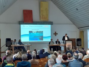 Foto von der B�rgerversammlung am 23.04.2026 im Martinstadl. Auf de B�hne 1. B�rgermeister; im Vordergrund B�rgerinnen und B�rger
