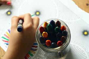 Kinderhand malt mit bunter Kreide ein Ausmalbild aus.