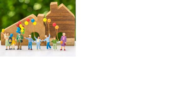 Personen bzw. Figuren  mit bunten Luftballons vor zwei Holzhäusern
