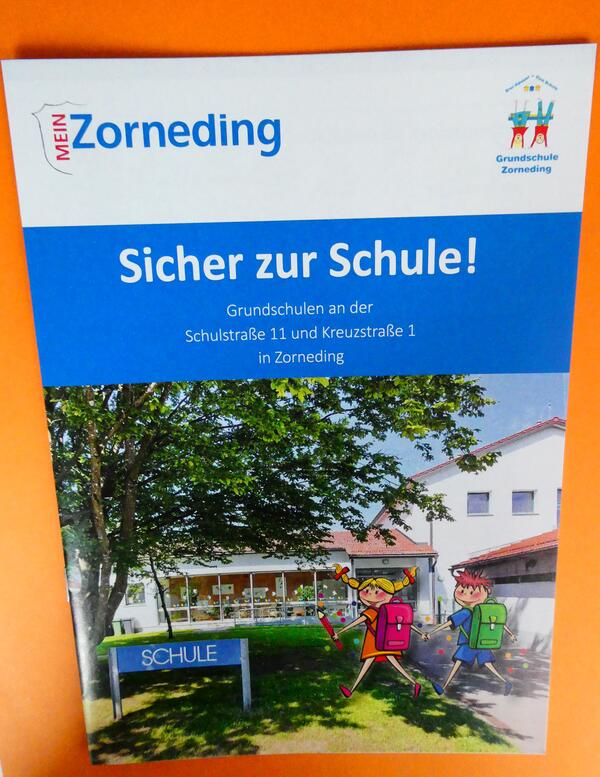 Titelbild der Broschüre "Sicher zur Schule" zu sehen ist die Grundschule Zorneding mit gemalten Kindern, die zur Schule gehen. 
